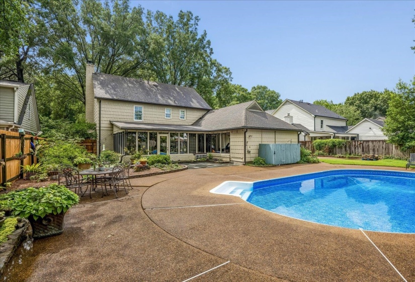 Exterior featuring an in-ground swimming pool with concrete surround, a screened-in porch, and mature landscaping