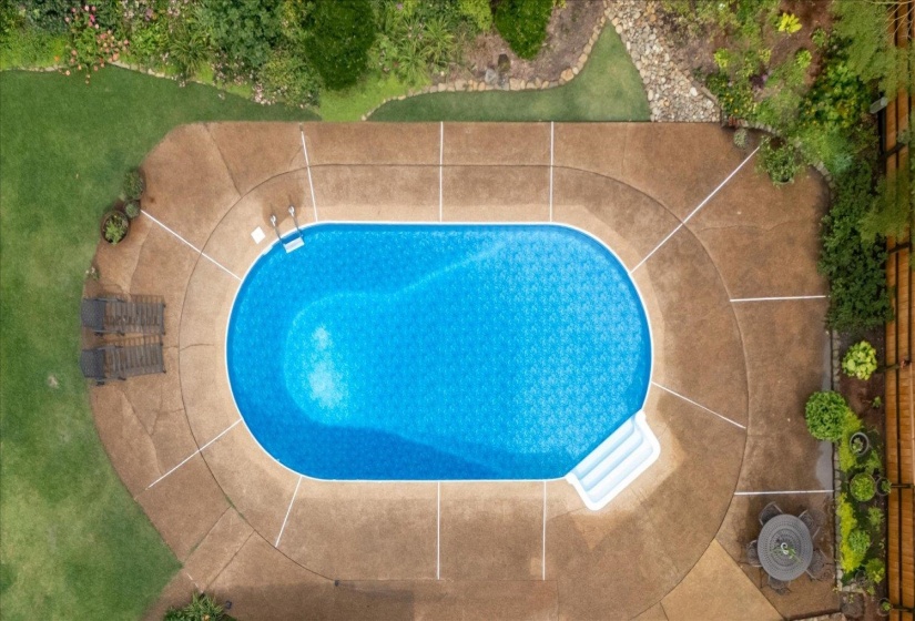 Oval-shaped in-ground swimming pool with integrated steps, surrounded by a textured concrete deck