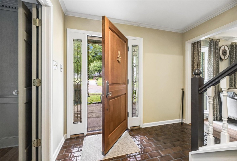 Entryway featuring a solid wood front door with decorative glass sidelights, terracotta-style floor tiling, light beige wall paint, and white crown molding