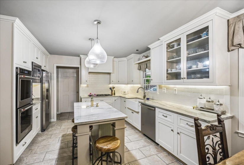 White shaker cabinetry with crown molding, stainless steel appliances, a center island with quartzite countertop seating, a farmhouse sink, and tile flooring