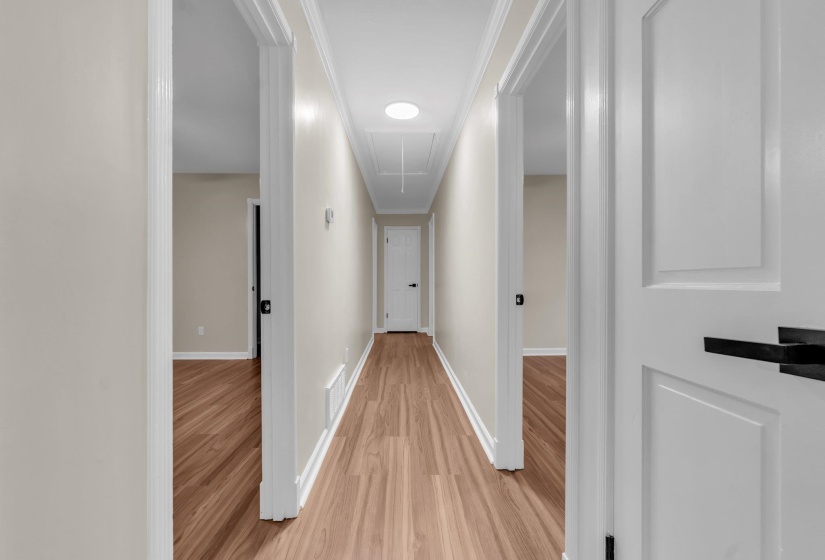 Hallway featuring wood-finish flooring, light neutral wall tones, white trim, and white panel doors with matte black hardware