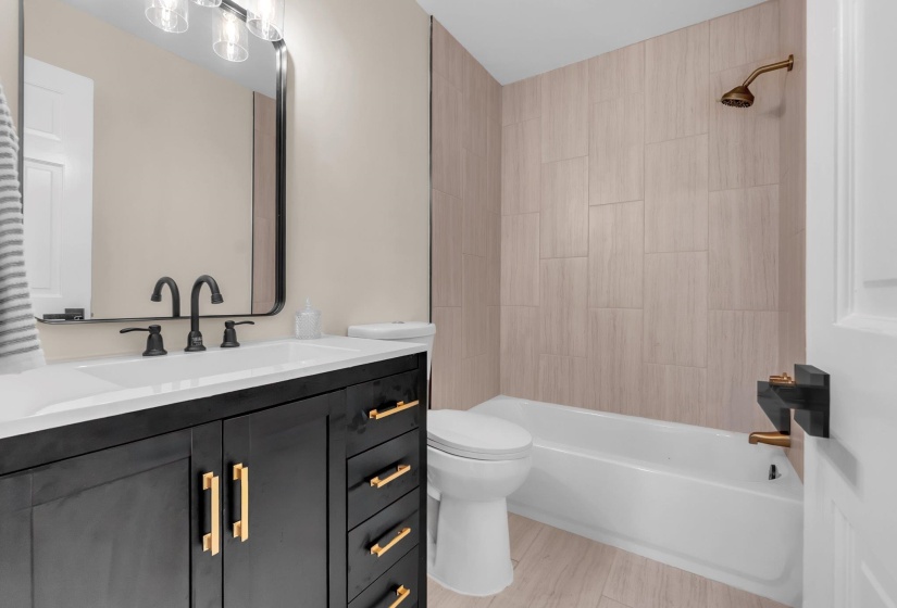 Modern bathroom featuring a dark wood vanity with gold-tone hardware, a white integrated sink, and matte black faucet