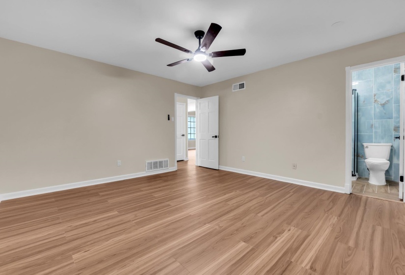 Spacious room featuring wood-finish flooring, light neutral wall tones, and a ceiling fan with integrated lighting
