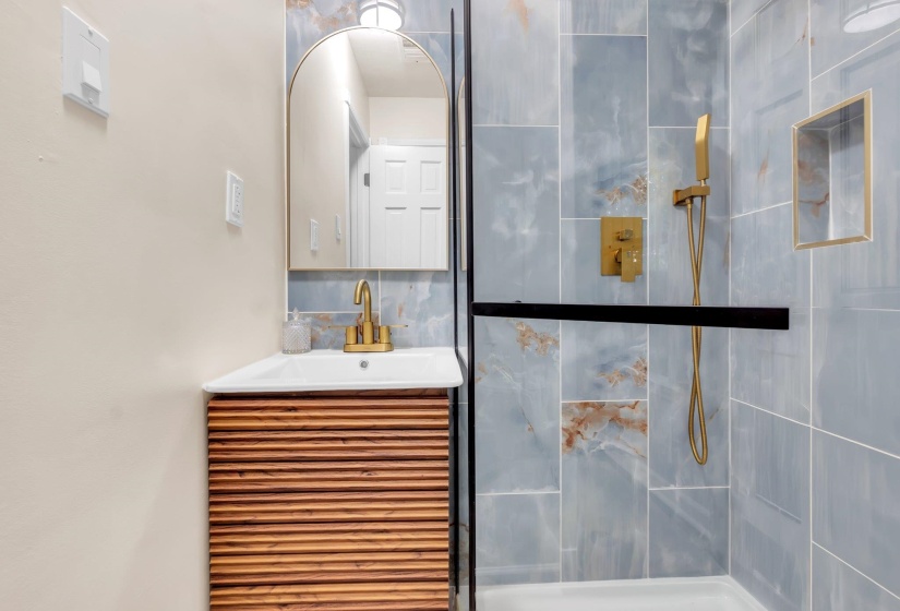 Contemporary bathroom featuring a wood-slat vanity, brass-finish fixtures, and a glass-enclosed shower with blue-toned tile