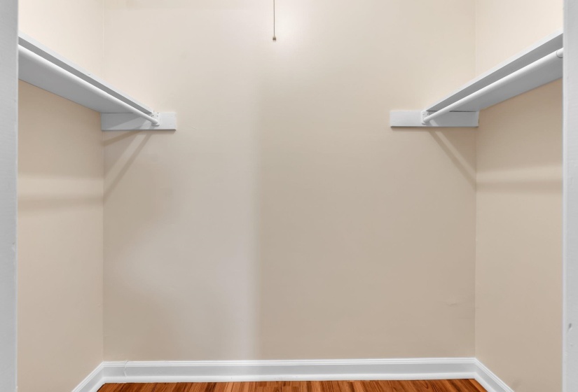 Spacious closet featuring two clothing rods, shelving, light cream wall paint, white baseboards, and wood-finish flooring
