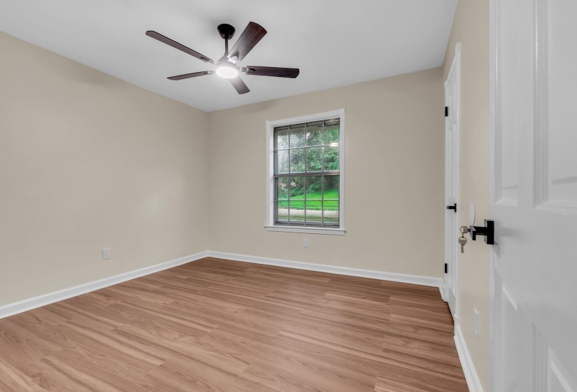 Spacious room featuring wood-finish flooring, a contemporary ceiling fan with integrated lighting, and a window with exterior views