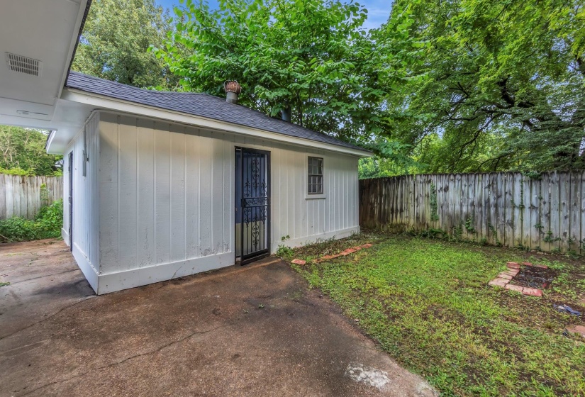 Rear exterior featuring white vertical siding, a black shingled roof, and a security screen door