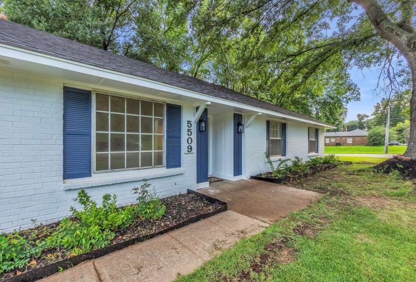 White painted brick exterior with blue shutters, a dark shingle roof, and a front entry with vertical siding