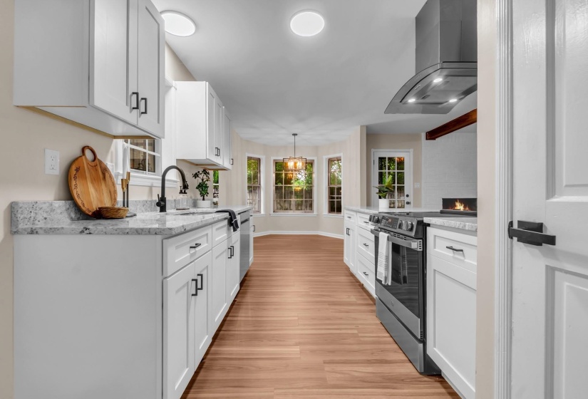 Kitchen featuring white cabinetry, light-toned countertops, wood-finish flooring, a stainless steel range hood, and a built-in electric fireplace