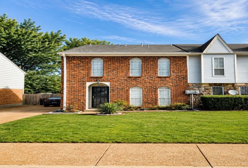 Brick and siding exterior featuring arched windows, a manicured lawn, and a paved walkway