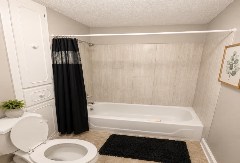 Bathroom featuring a white tub and shower combination with light-toned wall tiling, built-in cabinetry, and neutral wall paint