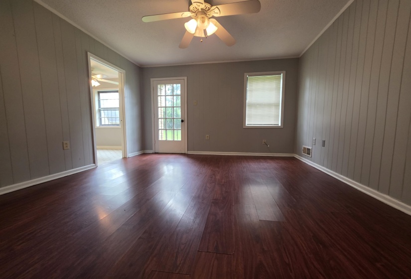 Interior room featuring dark wood-finish flooring, light gray vertical paneling, and a white ceiling fan with integrated lighting