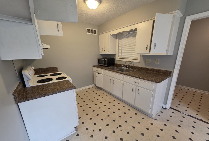 Kitchen featuring a double basin stainless steel sink, white cabinetry with silver hardware, speckled countertops, and a white electric range