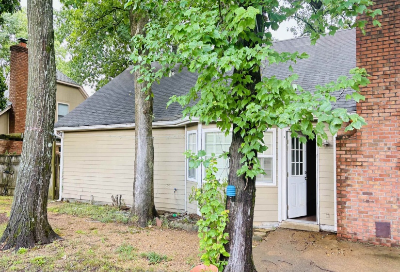 Rear exterior featuring tan horizontal siding, a dark shingle roof, a white multi-pane glass door, and a brick chimney