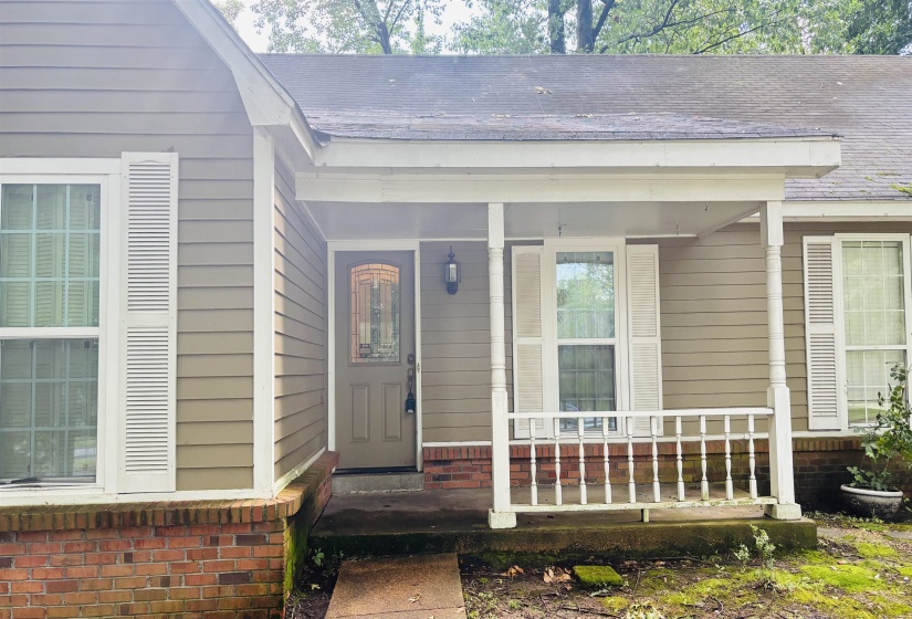 Covered front porch featuring a decorative railing and columns, a paneled front door with an arched glass insert, and neutral-toned siding with white window shutters