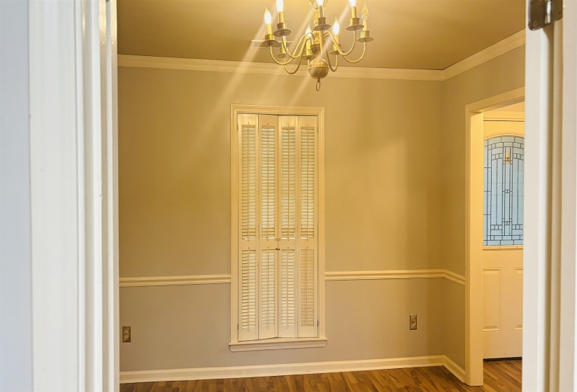 Dining area featuring wood-finish flooring, a brass chandelier, window with plantation shutters, and crown molding with chair rail detailing