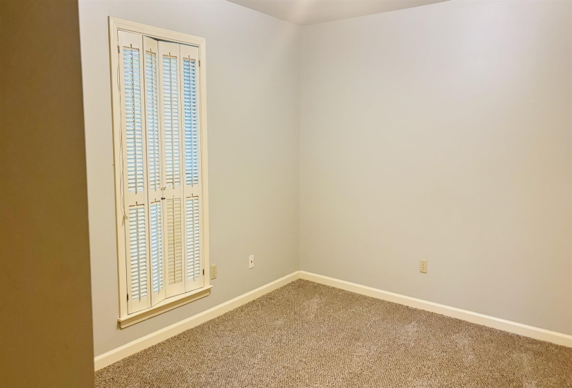 Room with neutral wall paint, light brown carpeting, white baseboards, and a window with white plantation shutters
