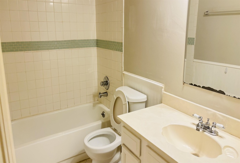 Bathroom featuring a built-in tub with tile surround, toilet, vanity with integrated sink, and wall-mounted mirror
