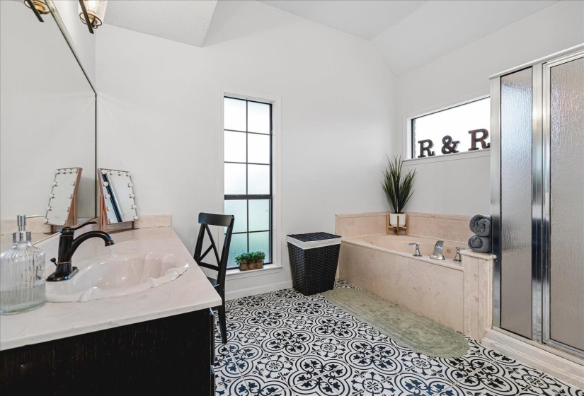Vaulted ceiling bathroom featuring patterned floor tiling, a built-in soaking tub, a stand-up shower with textured glass, a single vanity with a solid surface countertop, and multiple window features