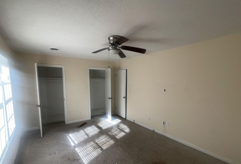 Room featuring two closet spaces with white doors, a ceiling fan with integrated lighting, and a large window with white blinds