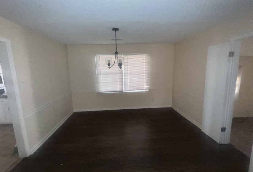 Spacious room featuring dark wood-finish flooring, light-toned walls with chair rail molding, and a central chandelier