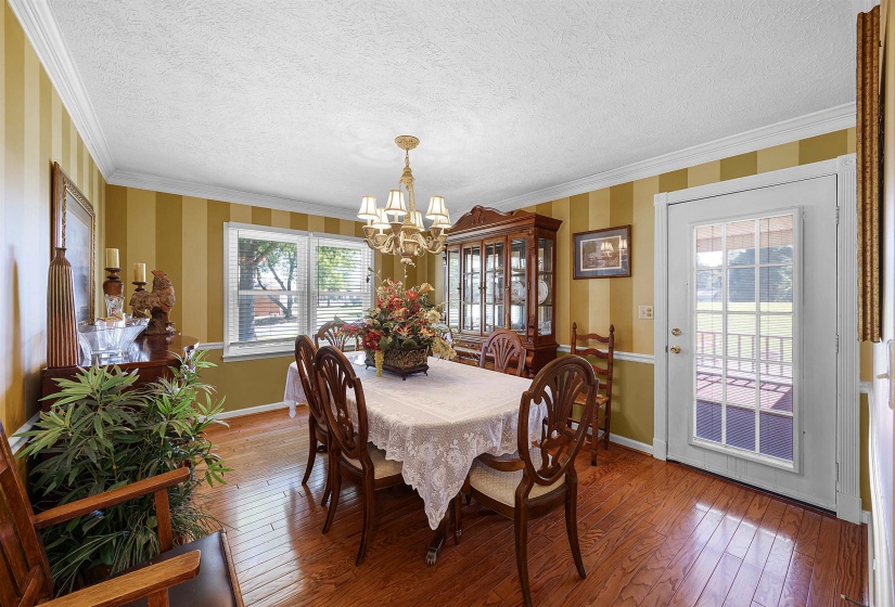 Dining space with wood-type flooring, crown molding, a textured ceiling, wallpapered walls, and a chandelier