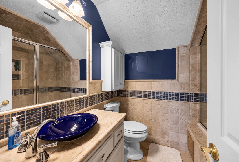 Full bathroom with tile walls, a shower stall, a textured ceiling, vanity, and wainscoting