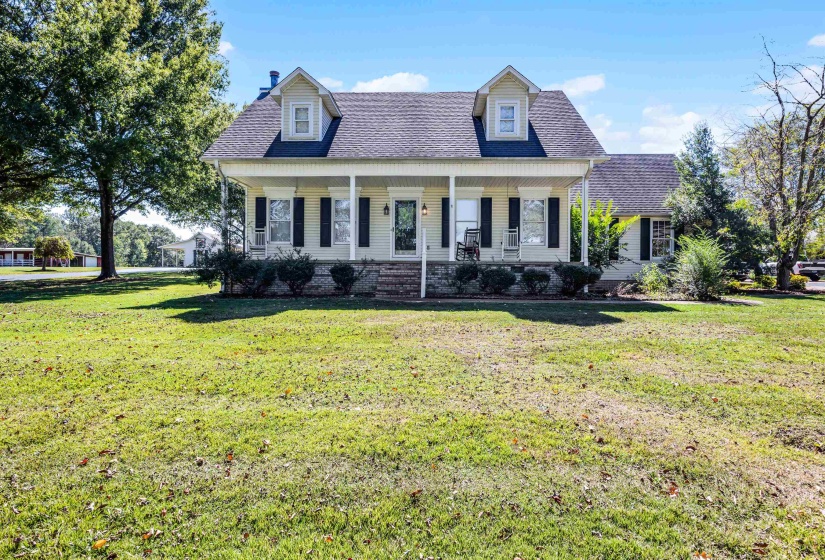 Cape cod home with roof with shingles, covered porch, a front lawn, and a chimney