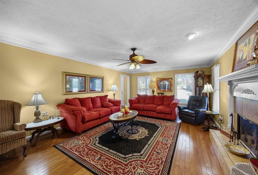 Living area featuring crown molding, wood-type flooring, a textured ceiling, a ceiling fan, and a tile fireplace