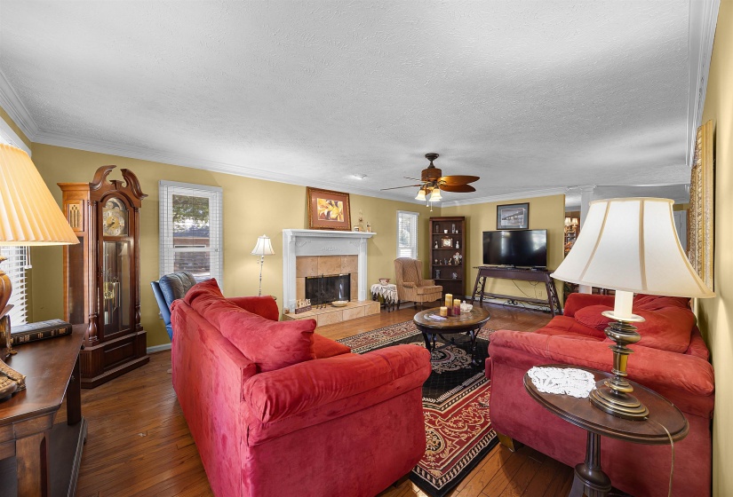 Living room featuring ornamental molding, a tiled fireplace, wood-type flooring, healthy amount of natural light, and a textured ceiling