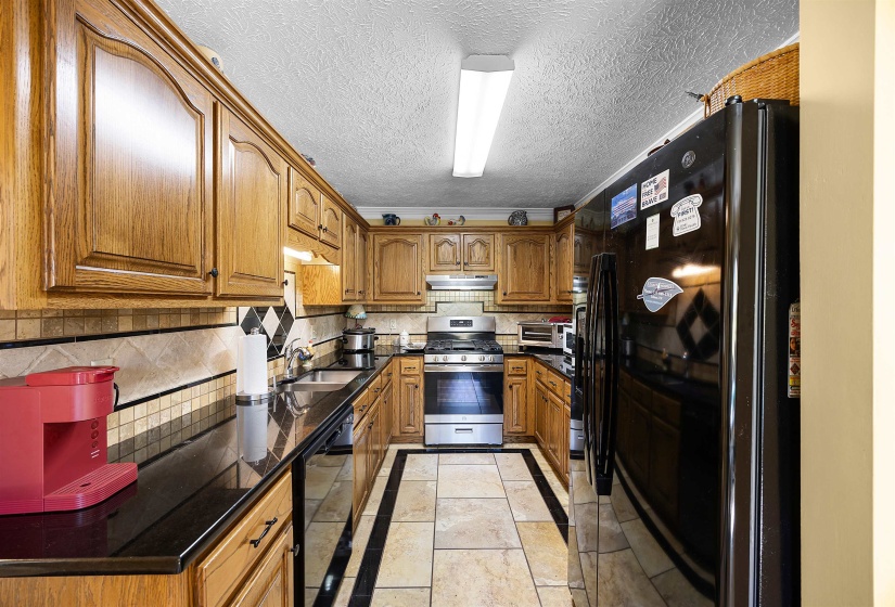 Kitchen featuring black appliances, brown cabinetry, backsplash, dark stone countertops, and a textured ceiling
