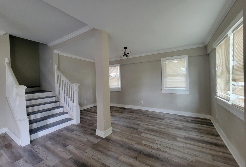 Unfurnished living room with crown molding, healthy amount of natural light, wood finished floors, baseboards, and stairway