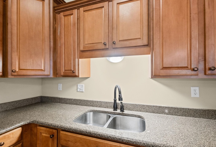 Kitchen area featuring wood cabinetry, speckled countertops, a stainless steel double basin sink, and a dark-finish pull-down faucet