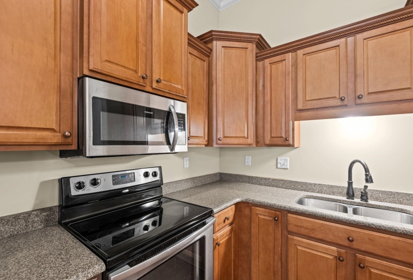 Kitchen featuring wood cabinetry, solid surface countertops, stainless steel sink with gooseneck faucet, black electric range, and stainless steel over-the-range microwave