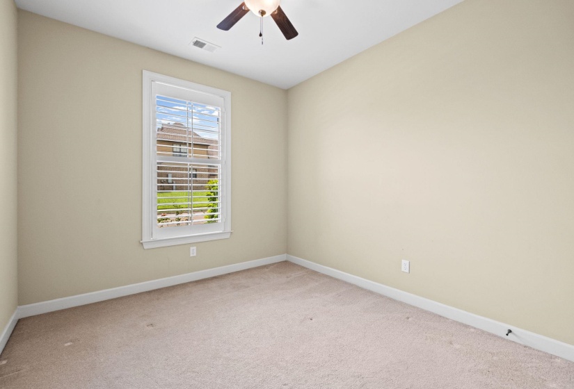 Neutral-toned room featuring a single window with white plantation shutters, carpeted flooring, and a ceiling fan with integrated lighting
