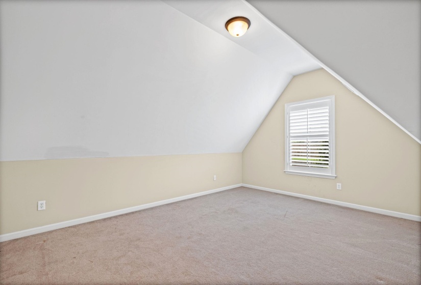 Carpeted room featuring a white window with plantation shutters, sloped ceilings, and a flush-mount ceiling light fixture