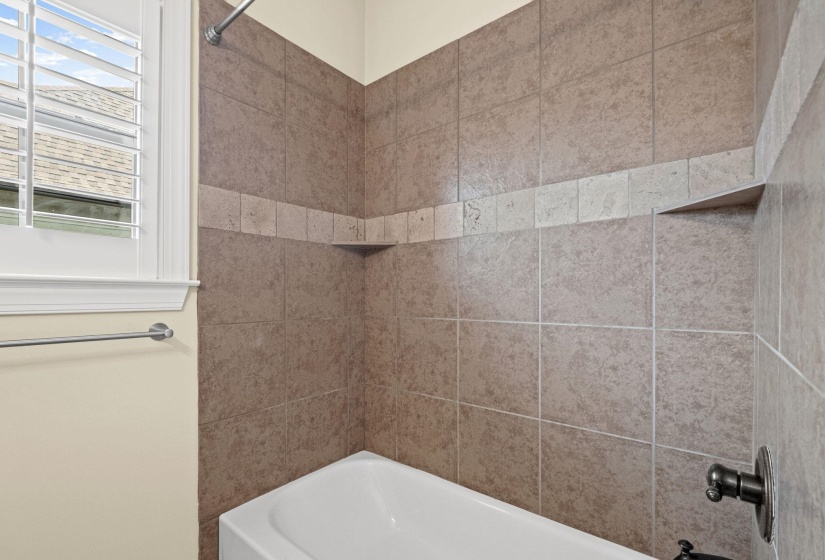 Tub and shower combination featuring earth-toned tile surround, decorative accent band, and an integrated corner shelf