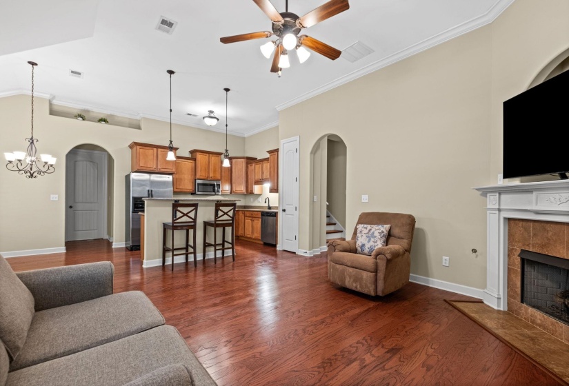 Spacious living area featuring wood-finish flooring, a ceiling fan, and a fireplace with a decorative mantel and tile surround