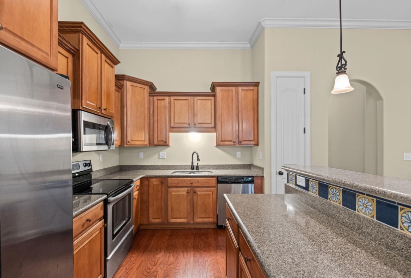 Kitchen featuring wood cabinetry, stainless steel appliances, speckled countertops, and wood-finish flooring