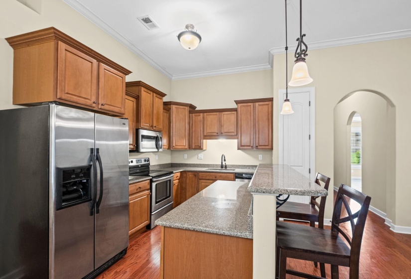 Kitchen featuring wood-finish cabinetry, stainless steel appliances, granite countertops, and a breakfast bar with pendant lighting