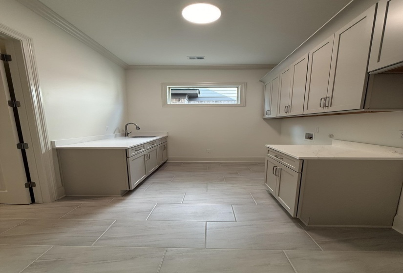Utility room featuring light grey cabinetry, white countertops, tile flooring, an undermount sink with a chrome faucet, and a rectangular window