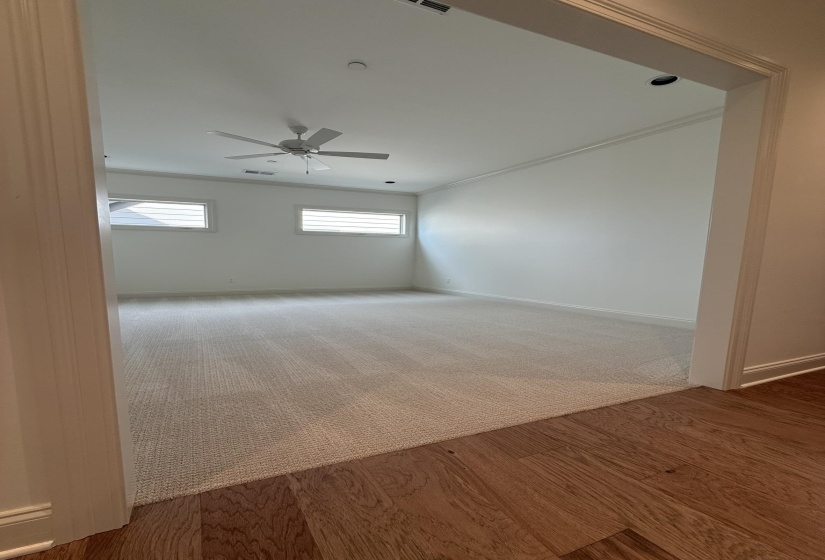 Spacious room featuring light-toned carpeting, white walls, and a ceiling fan