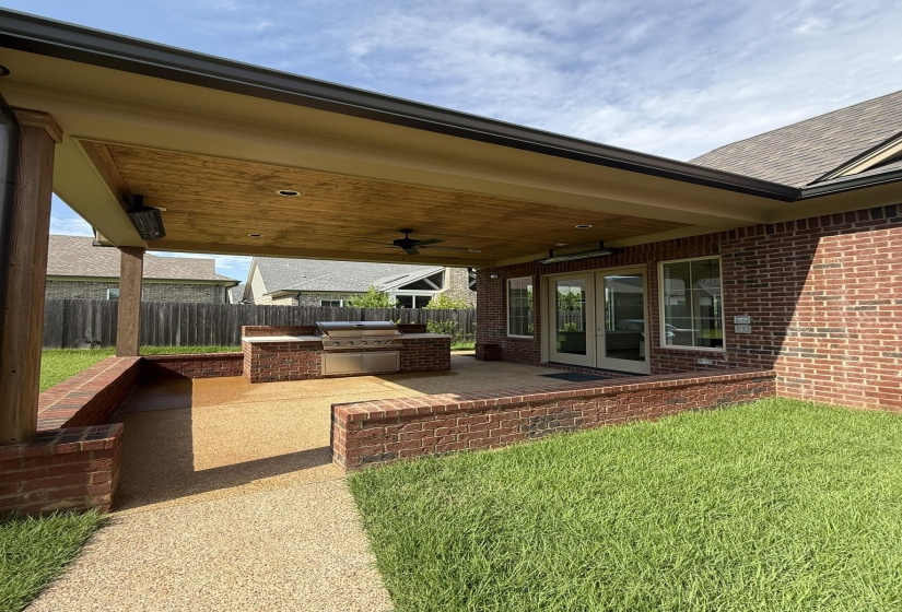 Covered patio featuring an integrated outdoor kitchen, brick half-walls, and textured aggregate flooring