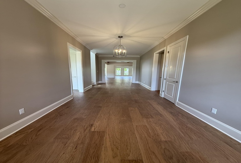 Long hallway featuring wood-finish flooring, white crown molding, and a drum pendant light fixture