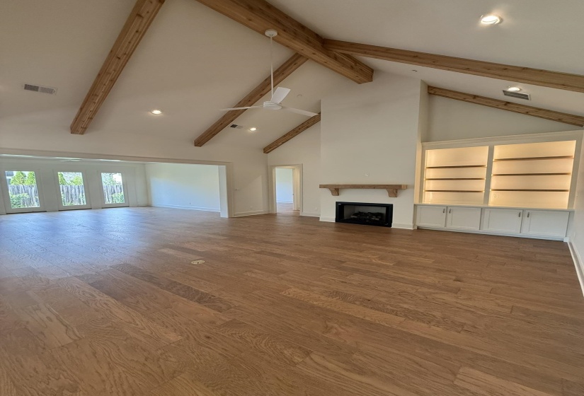Spacious living area featuring high vaulted ceilings with exposed wood beams, wood-finish flooring, a contemporary ceiling fan, and recessed lighting