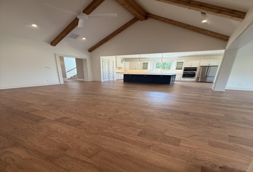 Open-concept living area featuring wood-finish flooring, a vaulted ceiling with exposed wooden beams, and recessed lighting
