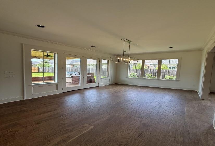 Spacious room featuring wood-finish flooring, ample natural light from multiple windows and French doors, a modern linear chandelier, recessed lighting, and crown molding