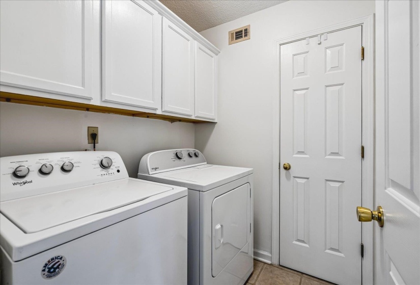 Utility area featuring white paneled upper cabinetry, neutral-toned floor tile, and a four-panel interior door with brass hardware