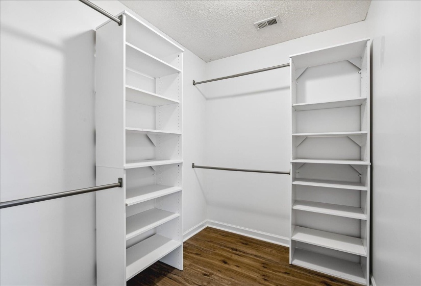 Walk-in closet featuring wood-finish flooring, white walls, built-in shelving units, and multiple clothing rods