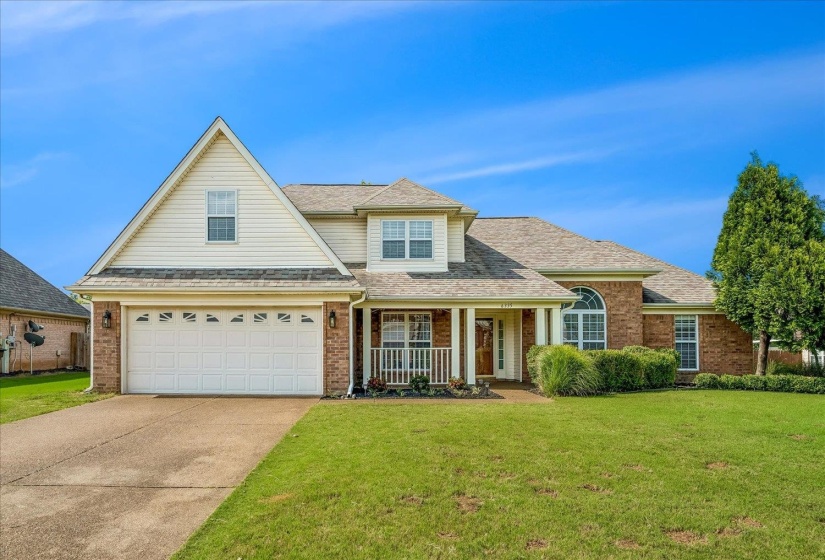 Brick and siding exterior featuring a covered front porch with white railing, a two-car garage, and an arched window accent
